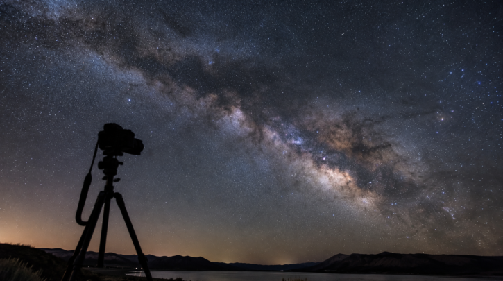 A camera on a tripod capturing the Milky Way over a landscape at night