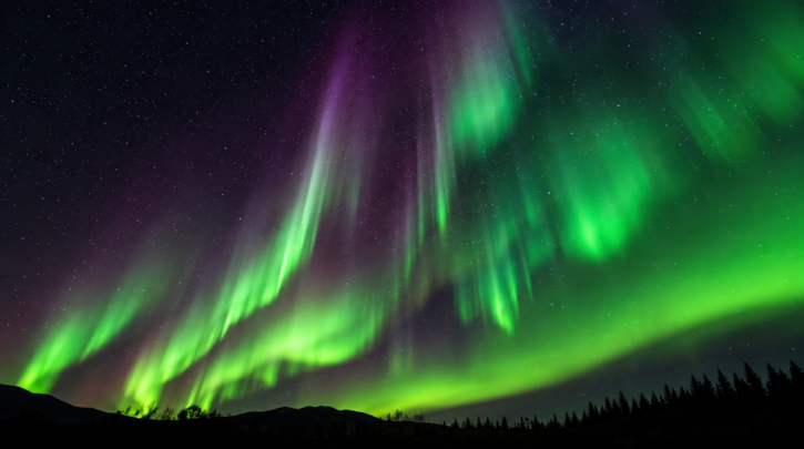 Green and purple aurora borealis curtains glowing over a dark landscape