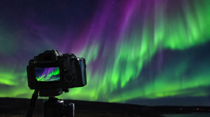 A camera on a tripod photographing an aurora display in the night sky