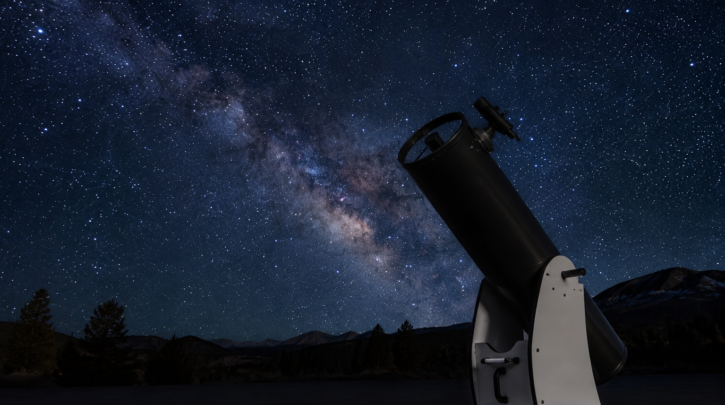 A large Dobsonian telescope set up under a dark, star-filled sky